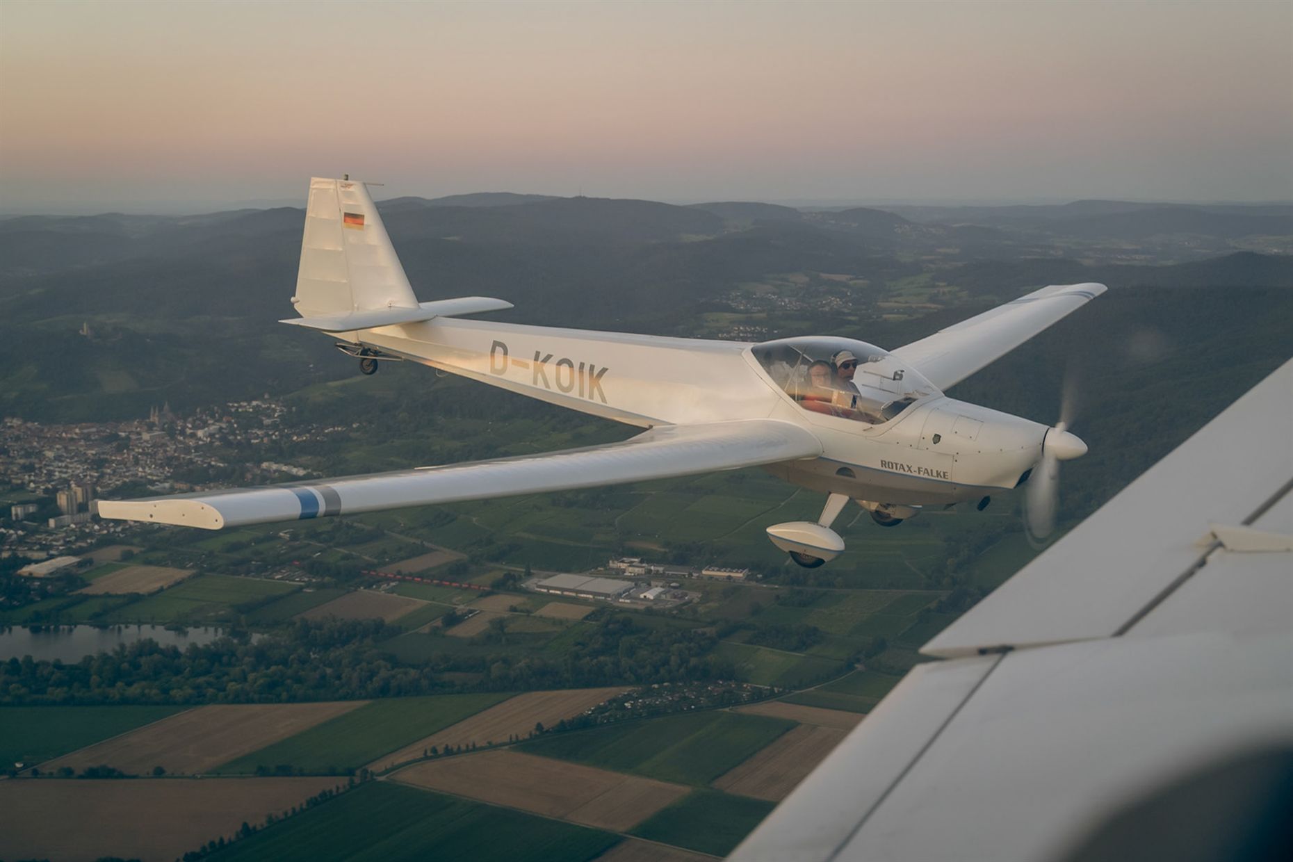 Segelflugzeug im Abendlicht über Hügeln und Feldern