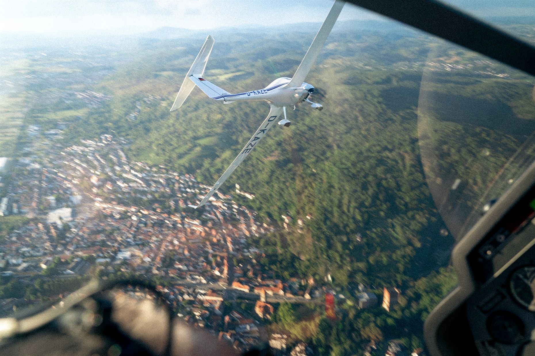 Segelflugzeug über einer Stadt und bewaldeten Hügeln