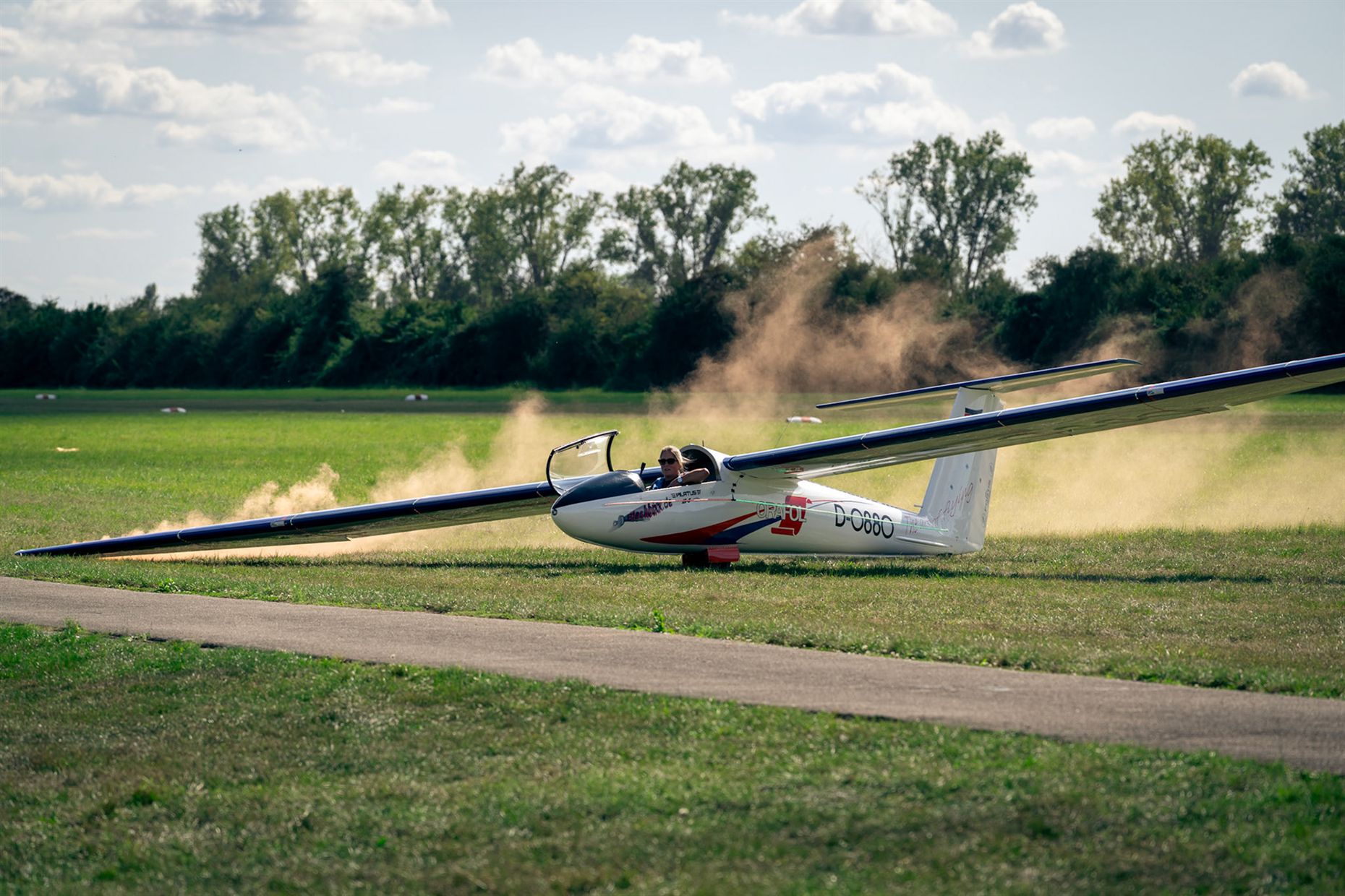 Segelflugzeug beim Start, hinter dem Flügel wirbelt Staub auf