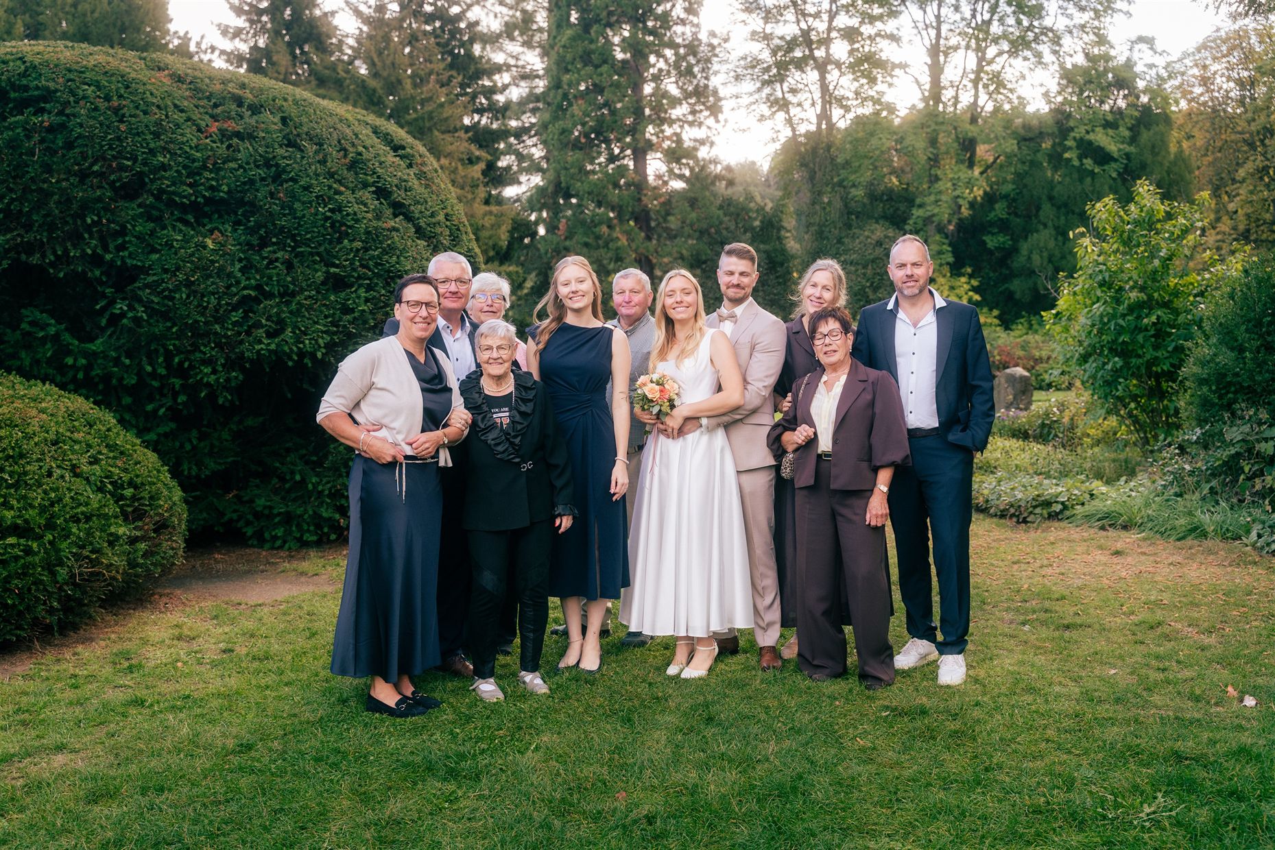 Familie und Brautpaar stehen gemeinsam im Park
